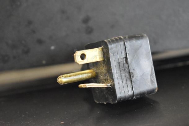 Close-up of a worn electrical plug with a black casing and brass prongs displaying visible signs of wear and tear.