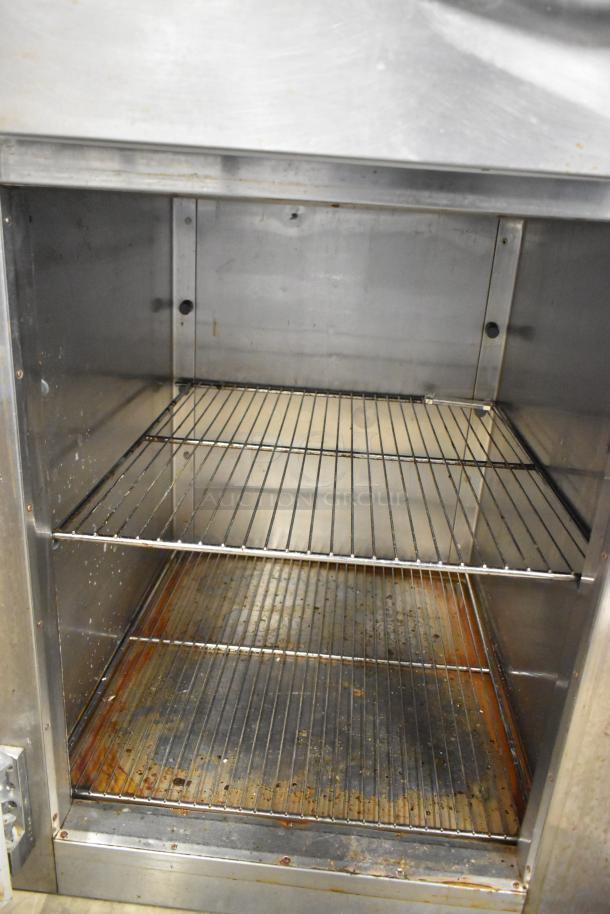 Traulsen stainless steel commercial cooler, 2 half-size doors, metal racks, 115V, 1 phase, visible wear.