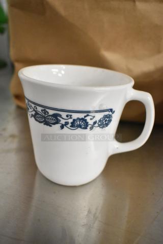 White ceramic mug with blue floral pattern, gently used condition. Part of a set of 8 mugs, enhancing bid value.