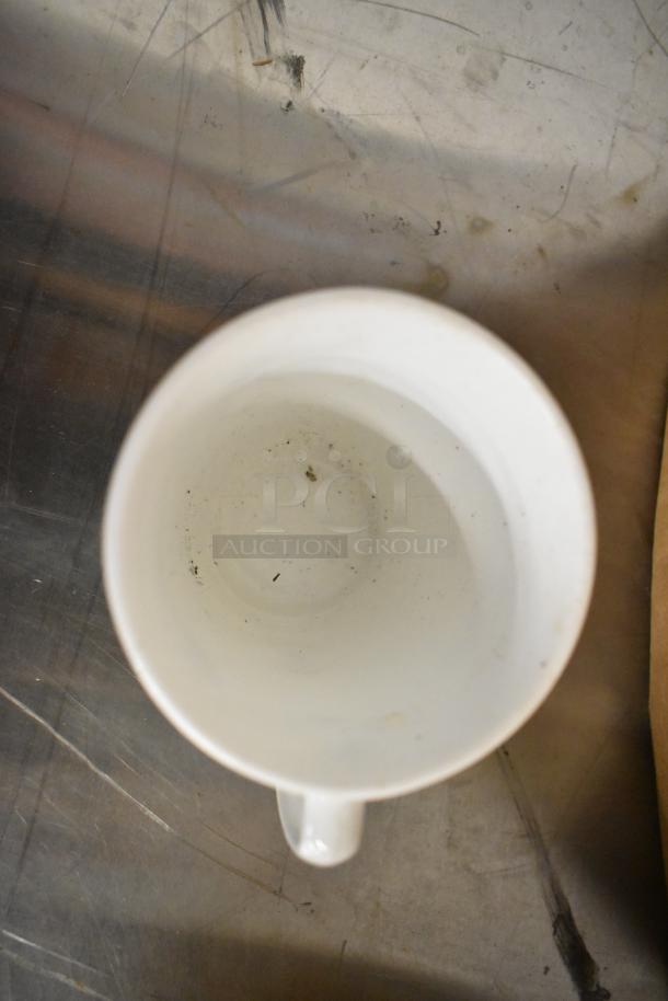 White ceramic mug, appears used with some interior marks. Auction includes 8 mugs in total.