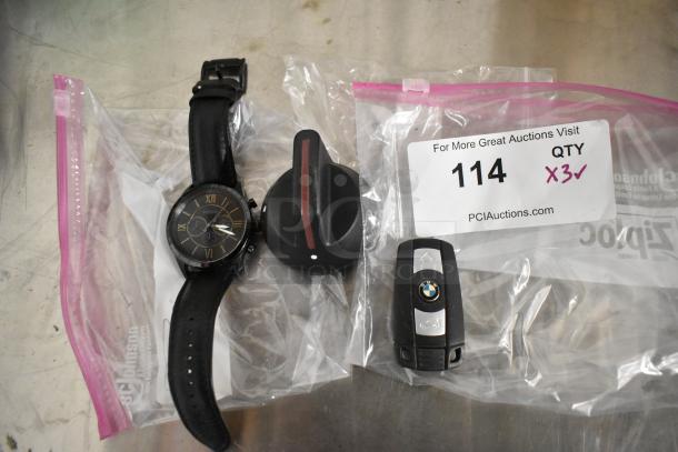 BMW key fob, Fossil watch, and knob in clear bags. Key fob has BMW logo. Watch features black leather strap. Auction tag reads "QTY 3x".