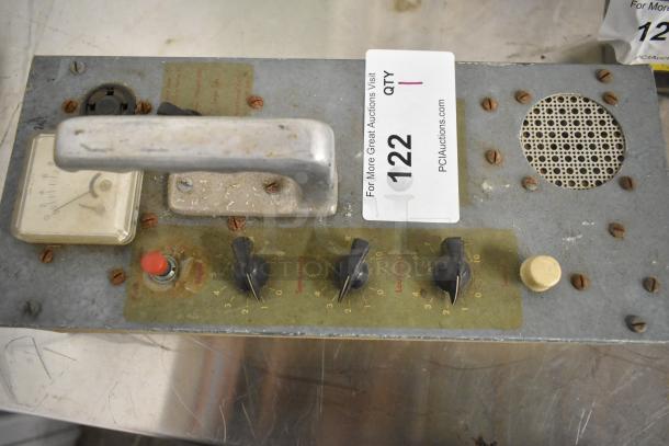 Vintage metal control panel with knobs, gauge, and handle, marked "122" for auction; shows signs of wear and rust.