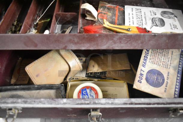Fishing tackle box with assorted contents, including hooks, lures, and manuals. Box shows signs of use, organized compartments.