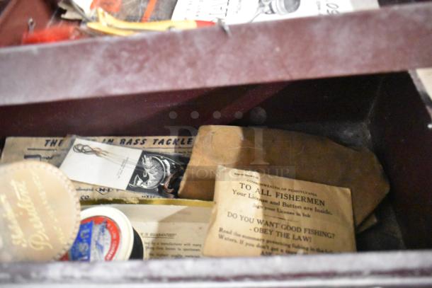 Vintage fishing tackle box with assorted contents, including various lures, hooks, and antique fishing licenses. Good condition.