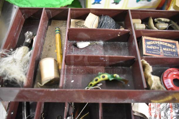 Brown fishing tackle box with assorted contents, including lures, line, safety matches, and a vintage wooden bobber.