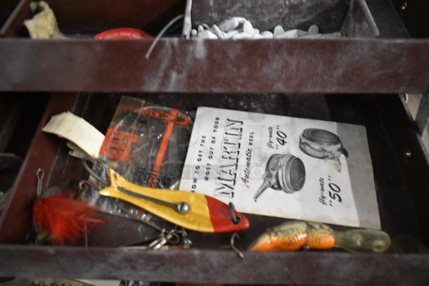 Fishing tack box with assorted lures, Martin reel booklet, and hooks. Well-organized, vintage condition.