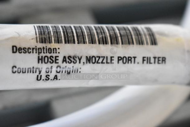 Hose assembly for oil filter with barcode tag, labeled "HOSE ASSY, NOZZLE PORT. FILTER," made in USA.
