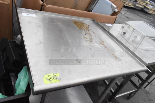 Stainless steel commercial table with metal under shelf, showing wear and rust. Mounted on commercial casters, item number visible.
