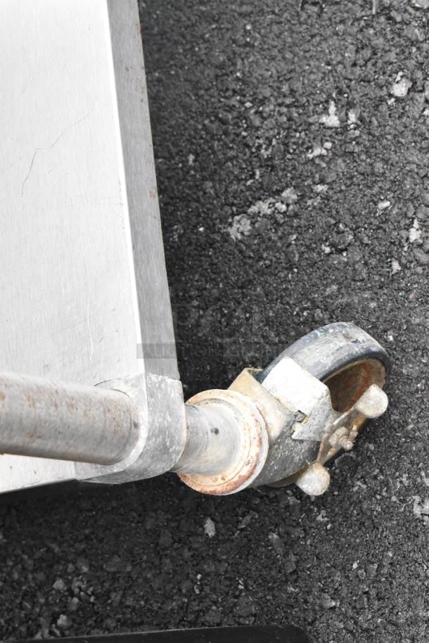 Stainless steel commercial table corner with metal under shelf on a commercial caster, showing minor rust and wear.