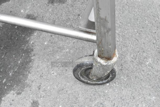 Metal pan transport rack with commercial casters, showing signs of wear. Sturdy construction for heavy-duty use.