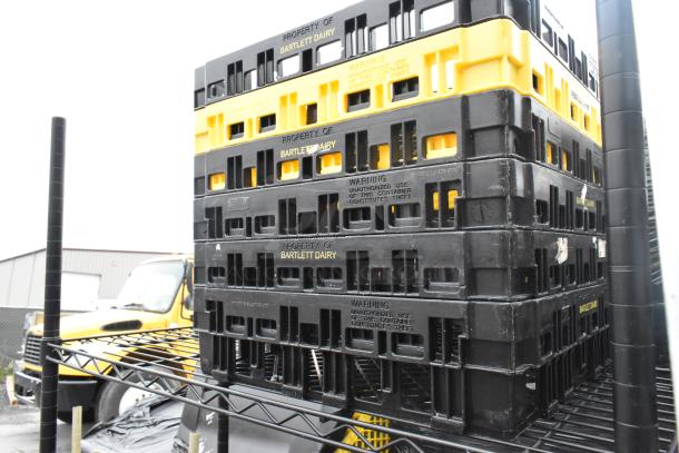 Black 4-tier wire shelving unit with a stack of Bartlett Dairy crates. Buyer must dismantle for shipping.