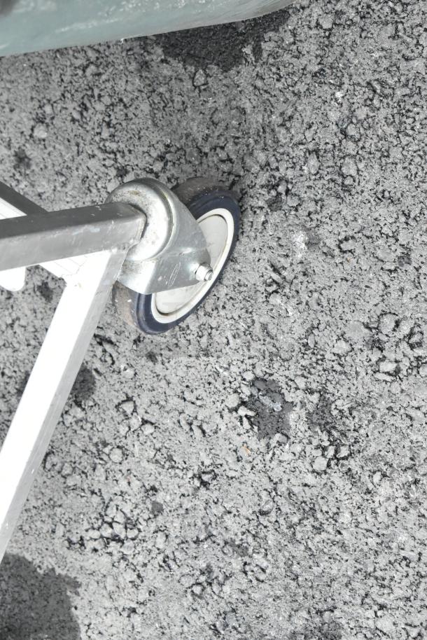 Metal commercial pan transport rack with sturdy commercial casters on a rough surface.