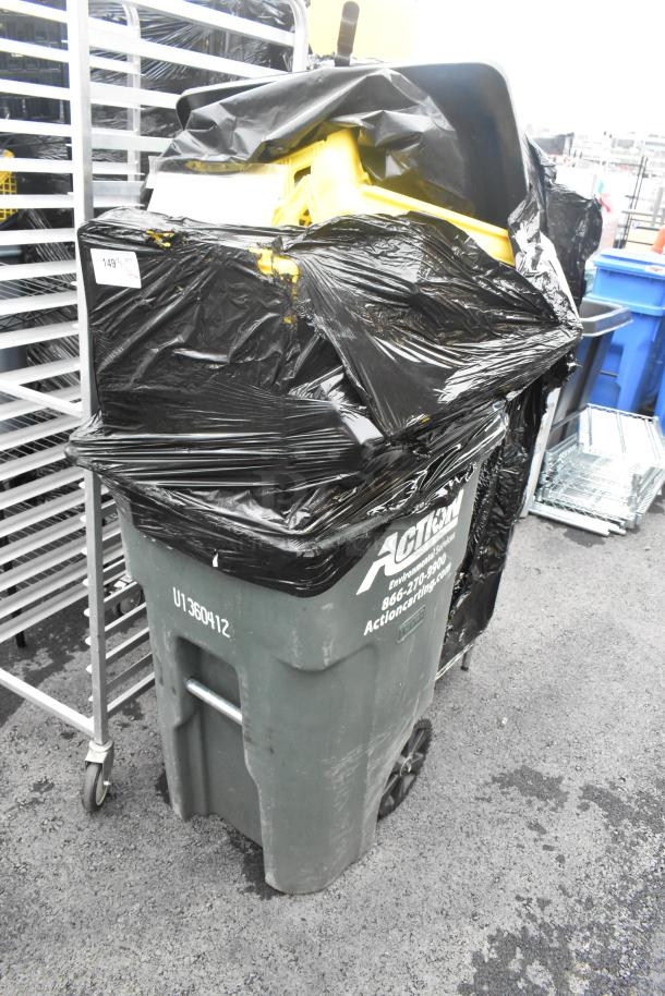 Green poly trash can storing bread caddies, wrapped in black plastic. Markings include "Action" contact info and "U1360412".