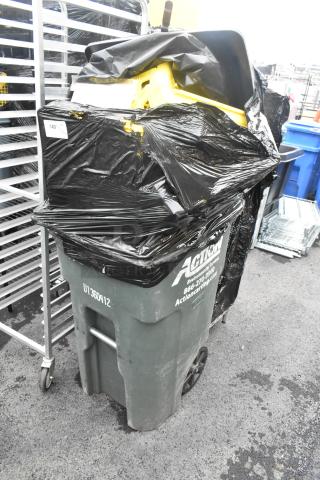Green poly trash can storing bread caddies, wrapped in black plastic. Markings include "Action" contact info and "U1360412".