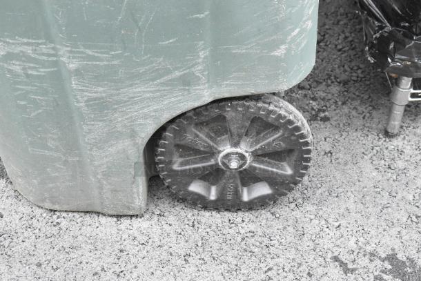 Poly trash can with visible wheel, showing signs of wear. Contains assorted bread caddies.