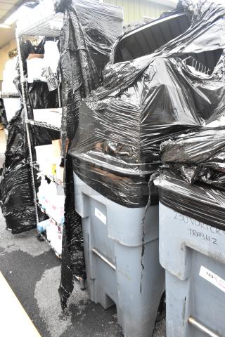Rubbermaid gray poly trash can filled with contents, including caddies; some wear and visible label markings.