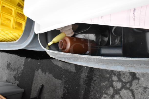 Rubbermaid gray poly trash can containing assorted items, including a yellow tool and brown bottle, with visible poly bin.
