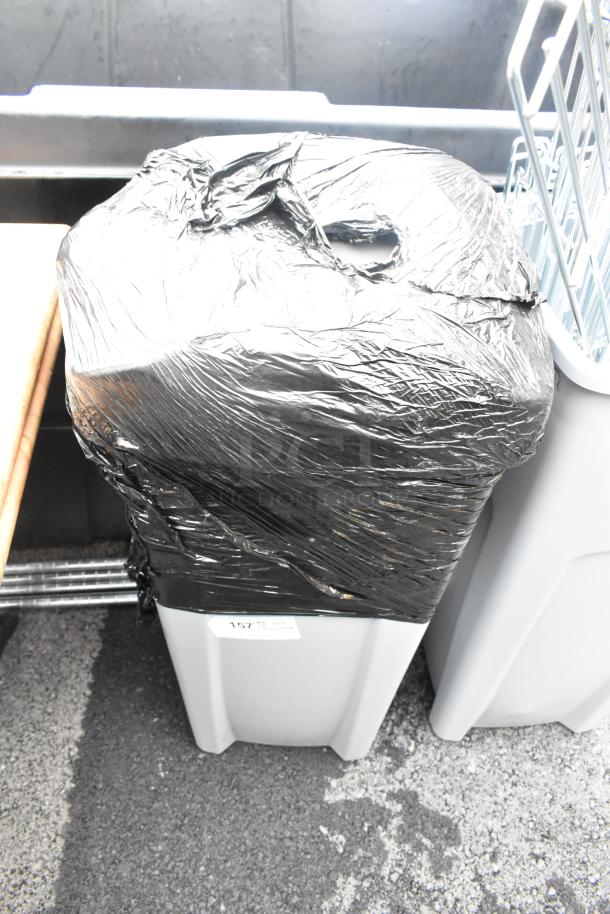 Gray poly trash can covered with a black plastic bag, labeled "157 Trash." Contains items including towels.
