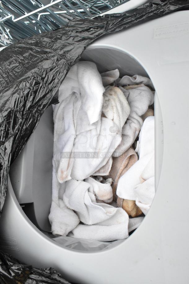 Poly trash can filled with white towels. Some towels appear stained. Black plastic bag lining inside.