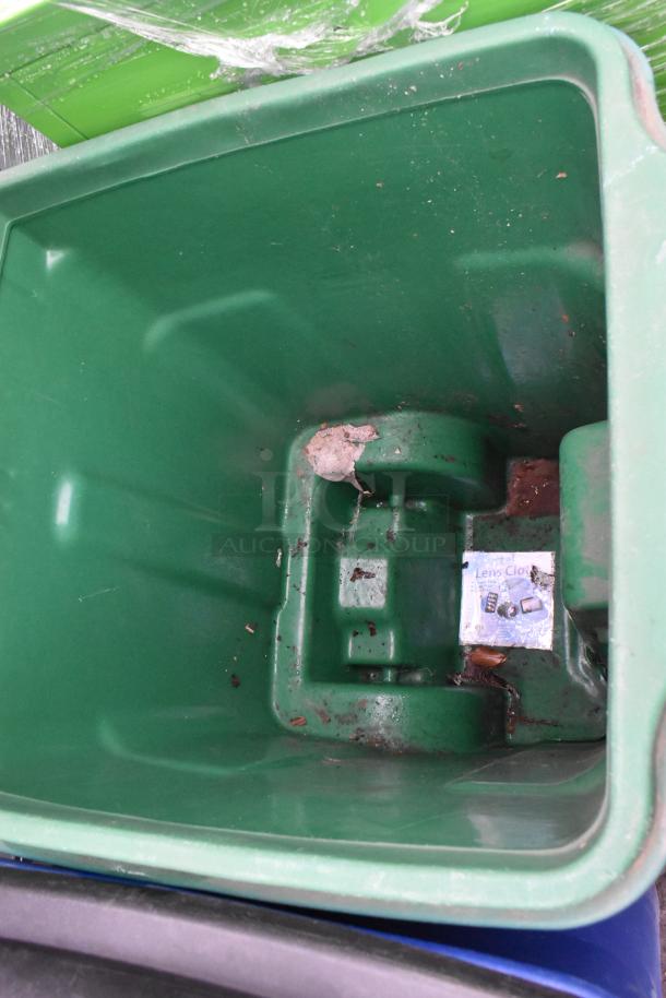 Two green poly trash cans with hinged lids, showing interior. Visible dirt suggesting used condition. Includes an additional item.
