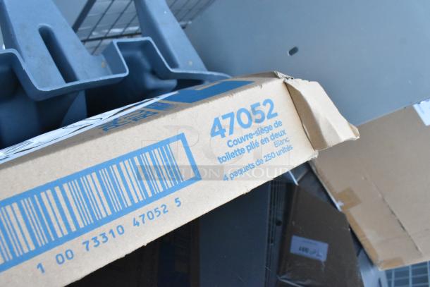 Gray poly trash can containing a red bucket and various items. Visible cardboard box labeled "47052," indicating toilet seat covers.