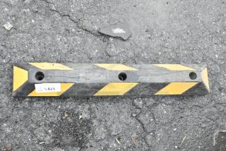 Black and yellow striped raised parking curb with visible mounting holes, slight wear, resting on asphalt.