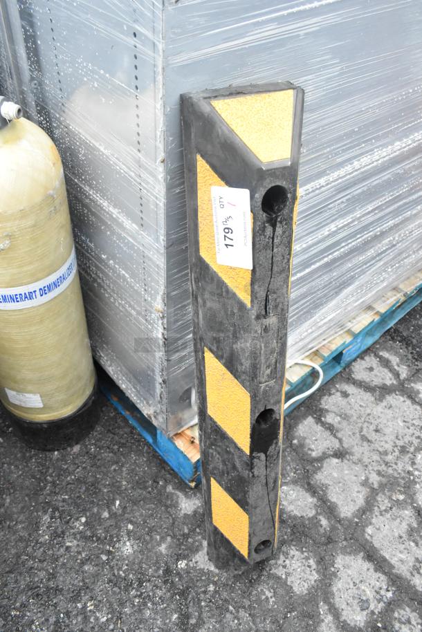 Raised parking curb in black with yellow reflective stripes, showing surface wear and pre-drilled mounting holes.