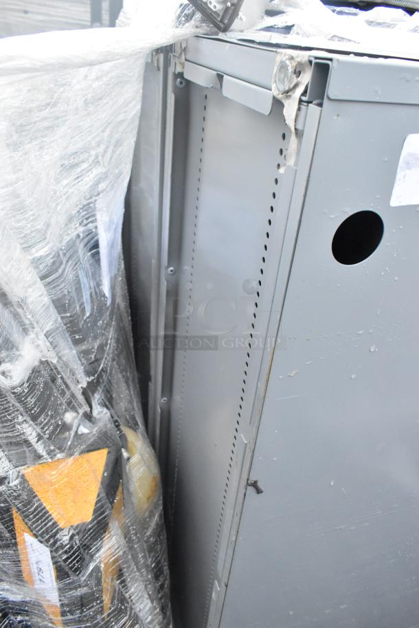 Gray metal shelving unit, partially wrapped in plastic, with visible perforations, slight wear, and a round hole on the side.