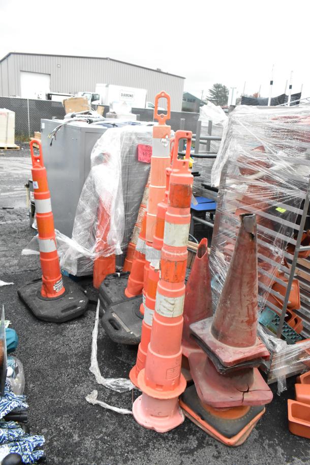 20 various orange poly cones in used condition, some with stripes, stacked outdoors. Ideal for traffic control or safety.
