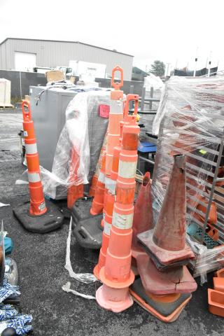 20 various orange poly cones in used condition, some with stripes, stacked outdoors. Ideal for traffic control or safety.