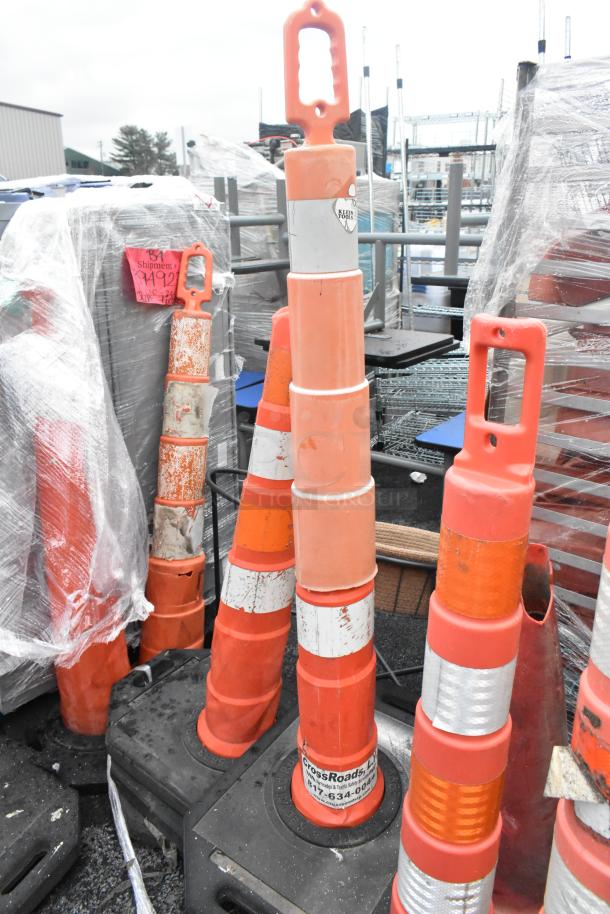 20 various orange poly cones with reflective stripes, stacked on black bases. Some show wear and labels indicating model and maker.