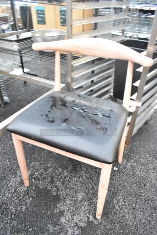 Wooden dining chair with natural finish and black seat cushion. Modern style, slightly wet surface, sturdy condition.