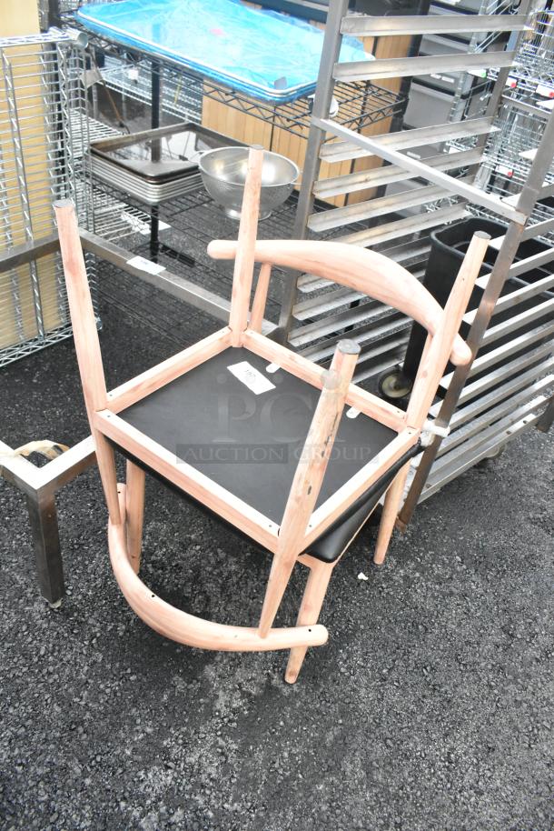 Two wooden dining height chairs with black seat cushions, natural finish, stacked. Minor wear visible.