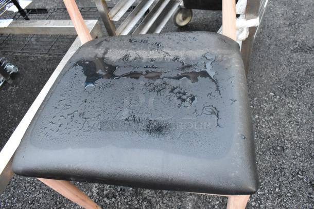 Wooden dining chair with black seat cushion, visible moisture on surface, natural wood frame. Good condition.