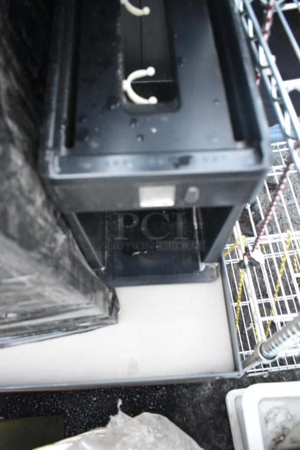 Black 1000930 cold brewer with visible water droplets, rectangular design, functional condition, on metal shelving.