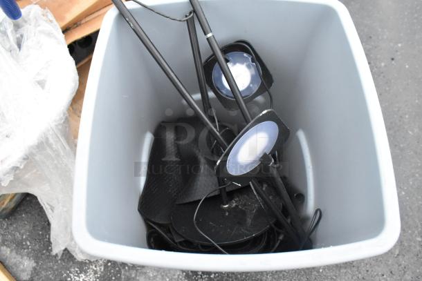 Rubbermaid gray poly trash can containing assorted black metal stands; appears used; durable construction.