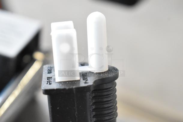 Close-up of a plug connector for the ServIt 423FW150 food warmer. Black base with white prongs, showing engraved markings.