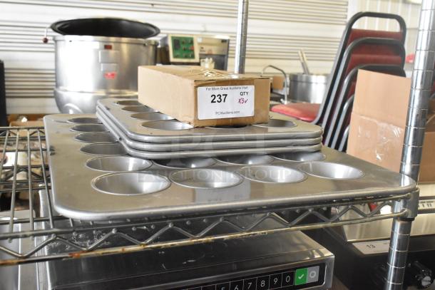 Stacked muffin baking pans in scratch and dent condition, with cardboard box labeled "237, QTY X5" on top, on metal shelving.