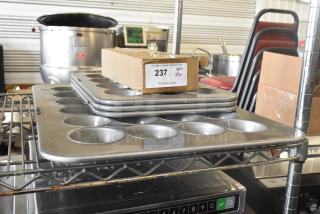 Stacked muffin baking pans in scratch and dent condition, with cardboard box labeled "237, QTY X5" on top, on metal shelving.