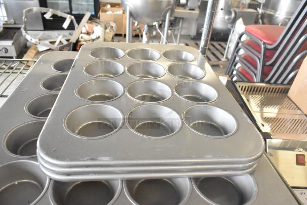Stack of new muffin baking pans with minor scratches and dents. Durable, non-stick, great for bulk baking.
