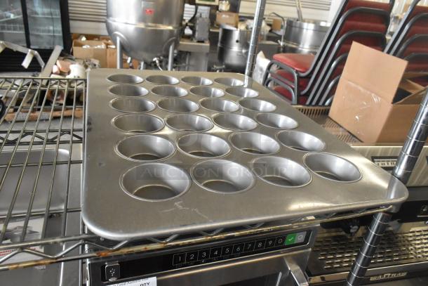 Brand new muffin baking pan with minor scratches, seated on metal rack. Ideal for kitchen use; part of scratch and dent sale.