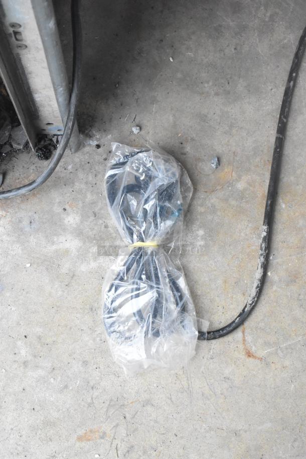 Plastic-wrapped power cord on a concrete floor next to a metal structure, part of Stoelting by Vollrath C111-37 soft serve machine.