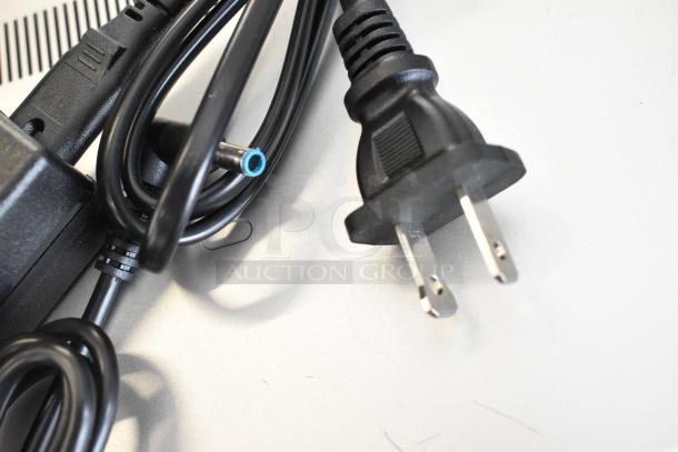 Close-up of an HP laptop charger cable with a standard two-prong plug, showing connector detail on a light surface.