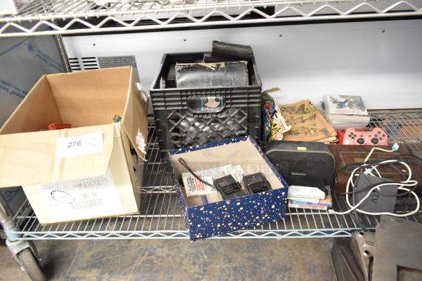 Tier lot including a Hess truck, figurines, Bible, Technics speaker, PS2 controllers, and various items on a metal shelf.