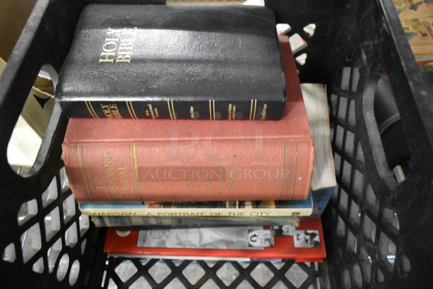 A stack of books in a crate, including a black Holy Bible and red legal manual, part of a mixed item auction lot.
