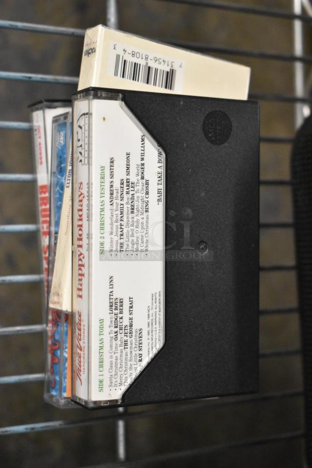 Tier lot with cassettes labeled "Happy Holidays," barcoded spine visible. Item includes Hess truck, figurines, Bible, Technics speaker, PS2 controllers.