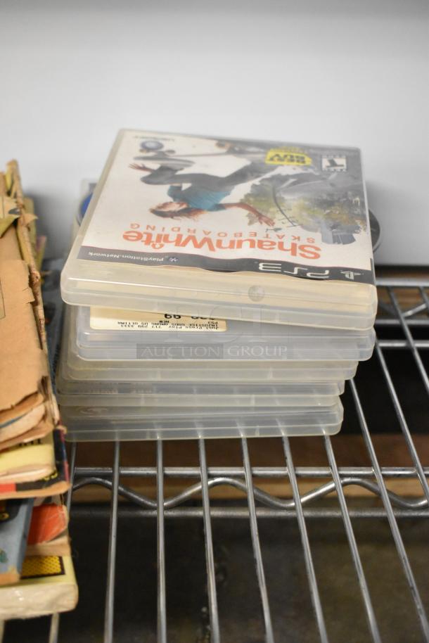 Stack of PS2 game cases, including "Shaun White Snowboarding," in used condition on a metal shelf.