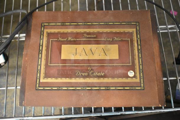 Wooden box labeled “Java by Drew Estate,” hand-made premium, on shelf. Includes visible wear.