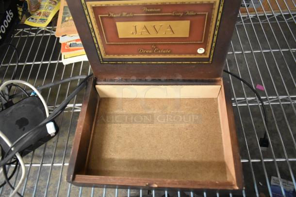 Open "JAVA by Drew Estate" cigar box on a metal shelf, showing label and empty interior.