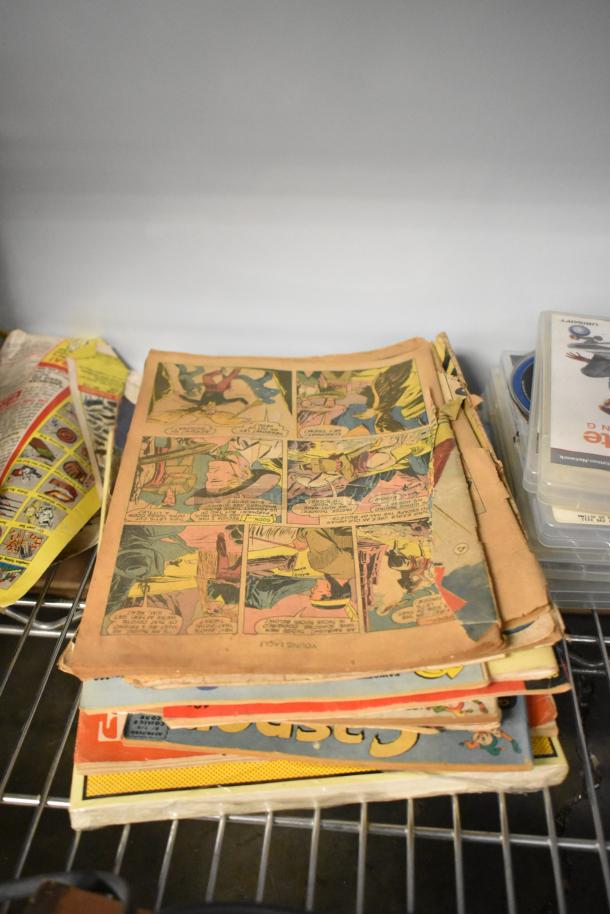 Stack of vintage comic books with worn edges on a metal shelf, part of an auction lot including Hess Truck and figurines.